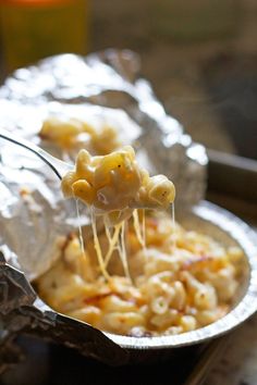 a spoon full of macaroni and cheese being lifted from a tin foil container