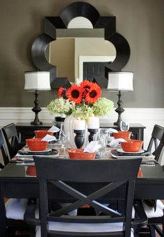 a dining room table with plates, cups and vases on top of it in front of a mirror