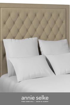 an upholstered headboard with white pillows and linens on the bottom bed