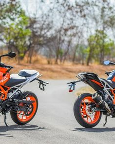 two motorcycles parked side by side on the road in front of some grass and trees