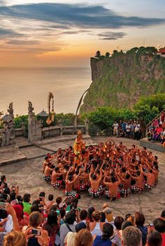 a group of people standing on top of a cliff next to the ocean and an audience