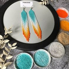 two pairs of beaded earrings are displayed on a tray next to three bowls of beads