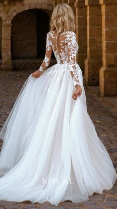 a woman in a white wedding dress standing on a cobblestone street with her back to the camera