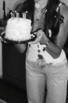 a woman holding a plate with a cake on it and candles sticking out of it