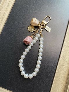 a keychain that is attached to a necklace with pearls and charms on it