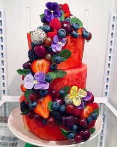 a three tiered watermelon cake with fresh fruit on top and purple flowers