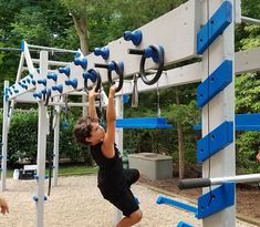 a young boy is climbing on a blue and white gym equipment set in the park