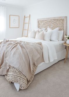 a bed with white linens and pillows in a neutral colored bedroom, along with a ladder