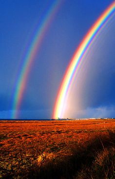 two rainbows are in the sky over an open field