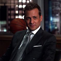 a man in a suit and tie sitting on a chair with a basketball behind him