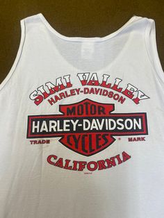 "Men's tank top Harley Davidson Moorpark Simi Valley, CA, 100% cotton, white color, size 3X. Good used condition, some stains and wear, check the pictures, official Harley Davidson product. Please, check carefully the measurements, photos and description of the article before buying it, we do not accept changes or returns. Measurements lying face down from outside: 28\" Across chest underarm to underarm. 15 1/2\" Shoulder seam to seam. 34\" Long, front middle top to bottom. Let me know if you ha Mens Tank, Simi Valley, Simple Shirts, Harley Davidson Motorcycles, Men's Tank, White Tank Top, White Tank, Mens Tank Tops, White Color