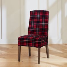 a red and black plaid chair sitting on top of a hard wood floor next to a white wall