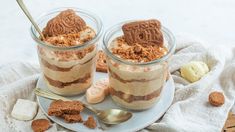 two glass jars filled with desserts on top of a white plate next to a spoon