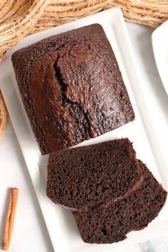 two slices of chocolate cake on a white plate with cinnamon sticks next to it,