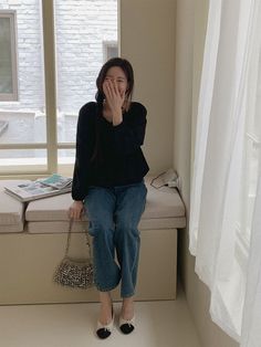 a woman sitting on a window sill with her hand in her mouth and looking out the window