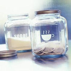 two glass jars filled with coffee beans and sugar on top of a table next to one another