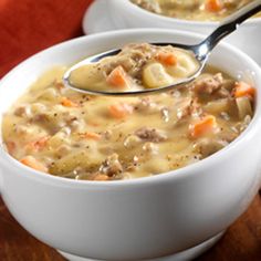 two white bowls filled with soup sitting on top of a wooden table next to a spoon