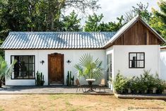 a white house with a metal roof surrounded by greenery and potted palm trees