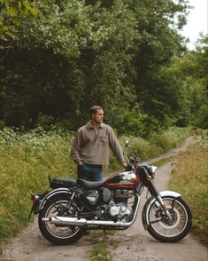 a man standing next to a motorcycle on a dirt road