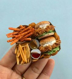 a hand holding a miniature hamburger and french fries