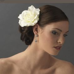 a woman with a flower in her hair wearing earrings and a white rose in her hair