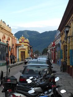 motorcycles are parked on the side of the road in front of buildings with mountains in the background