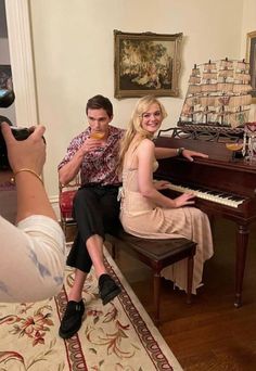 a man and woman sitting at a piano taking pictures with their cell phones as they pose for the camera