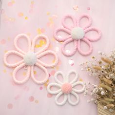 three pink and white hair clips sitting on top of a table next to dried flowers