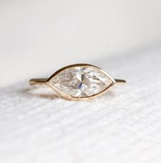 a diamond ring sitting on top of a white cloth covered surface with the center stone in gold