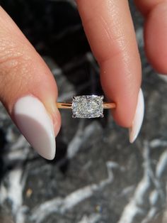 a woman's hand holding a ring with a diamond on it and white nail polish