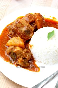 a white plate topped with rice and meat covered in gravy on top of a wooden table