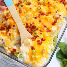 a person holding a wooden spoon over a casserole dish with cheese and bacon