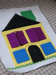 a house made out of paper sitting on top of a piece of white paper with purple and green felt