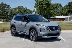 a silver nissan suv parked in a parking lot with trees and grass behind the car