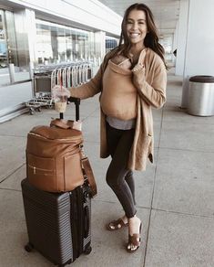 a pregnant woman is standing next to her luggage and smiling at the camera while posing for a photo