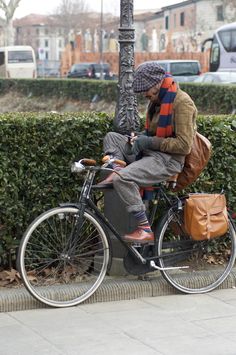 a man sitting on the back of a bike next to a street sign and tree