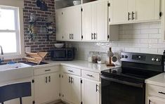 a kitchen with white cabinets, black appliances and a brick wall behind the stove top oven