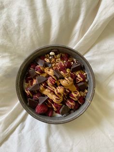 a bowl filled with chocolate, raspberries and other toppings on top of a white sheet