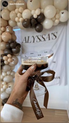 a person holding up a drink in front of balloons