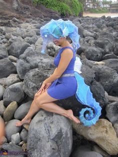 a woman in a blue dress sitting on some rocks