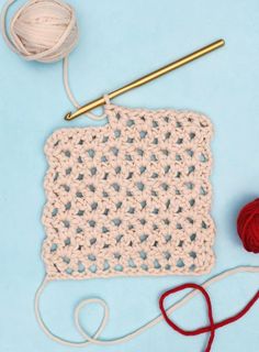 a crochet square with yarn and a knitting needle on a blue surface next to it