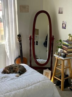 a cat laying on top of a bed next to a mirror and table with books