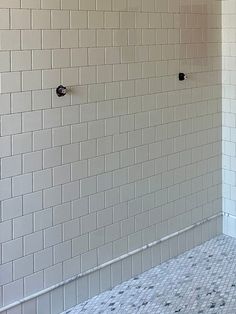 an empty bathroom with white tile and black handles on the shower wall, next to a tiled floor