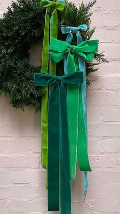 a green wreath hanging on the side of a white brick wall with ribbons tied around it