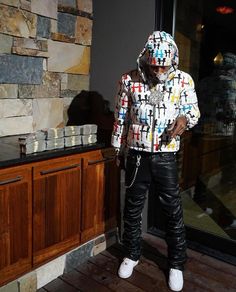 a young man standing in front of a window wearing a colorful jacket and black pants