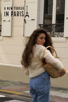 a woman is walking down the street carrying a wicker basket in her right hand