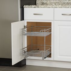 an open cabinet door in a kitchen with white cabinets and stainless steel baskets on the bottom shelf