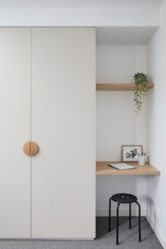 a white closet with two shelves and a black stool in front of it, next to a plant