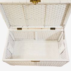 an open white wicker trunk with gold handles and latches on the lid is shown against a white background