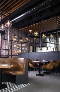 an empty restaurant with wooden booths and round tables in front of black walls, checkered flooring and glass globes hanging from the ceiling